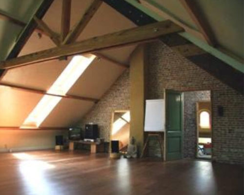 Afbeelding van de kleine zaal in De Verscholen Tuin in Deurne. Je ziet een planken vloer en oude houten dakgebinten.